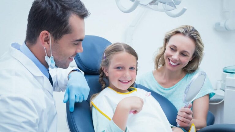 A happy family of four sitting together in a dental office smiling with a dentist
