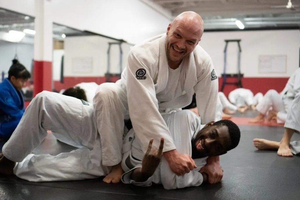 Two athletes practicing Brazilian Jiu-Jitsu grappling on mats inside a training gym