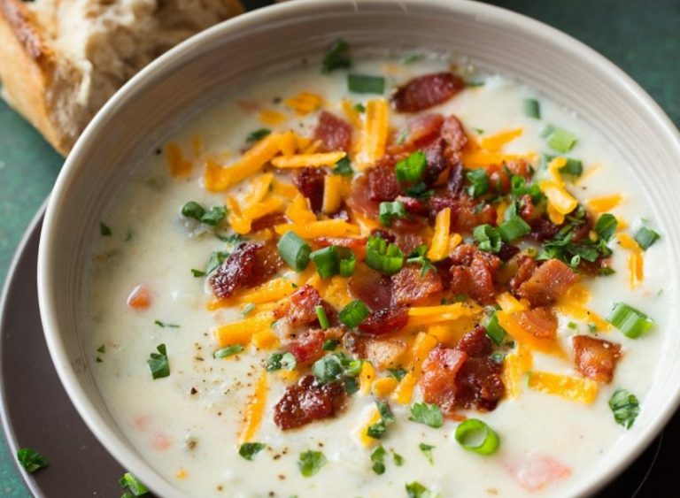 A steaming bowl of creamy potato soup topped with chives and crumbled bacon on a rustic table.